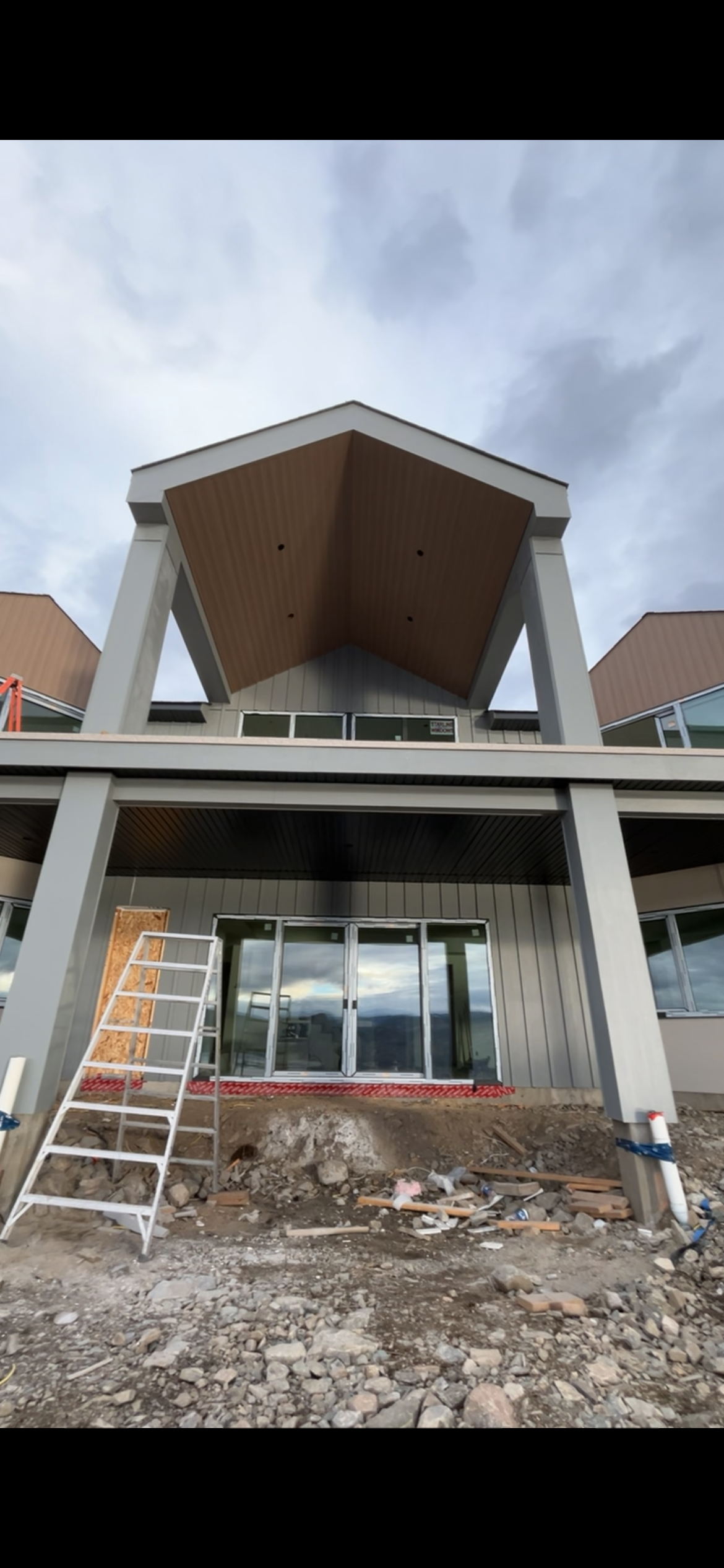 Residential exterior under construction with a vaulted wood-look soffit, grey columns and vertical siding